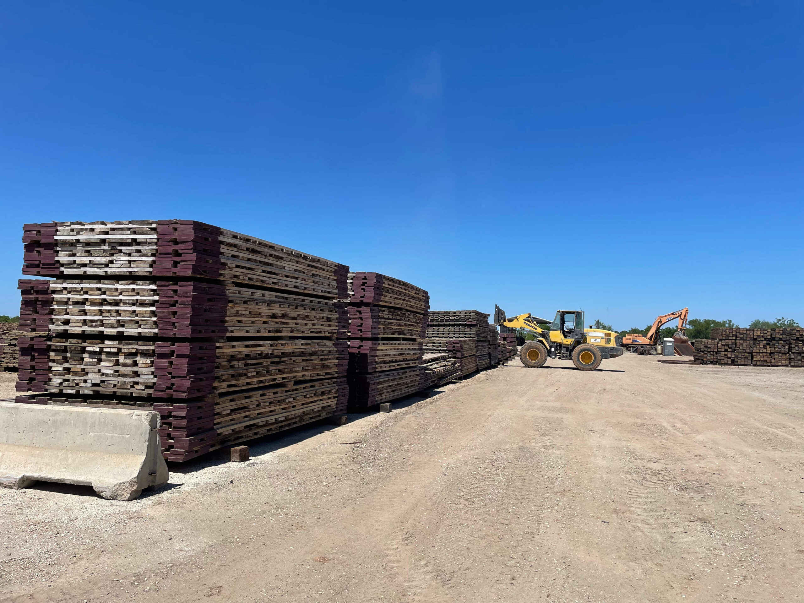 Stock of 3ply laminated mats in crane mat yard with yellow crane.