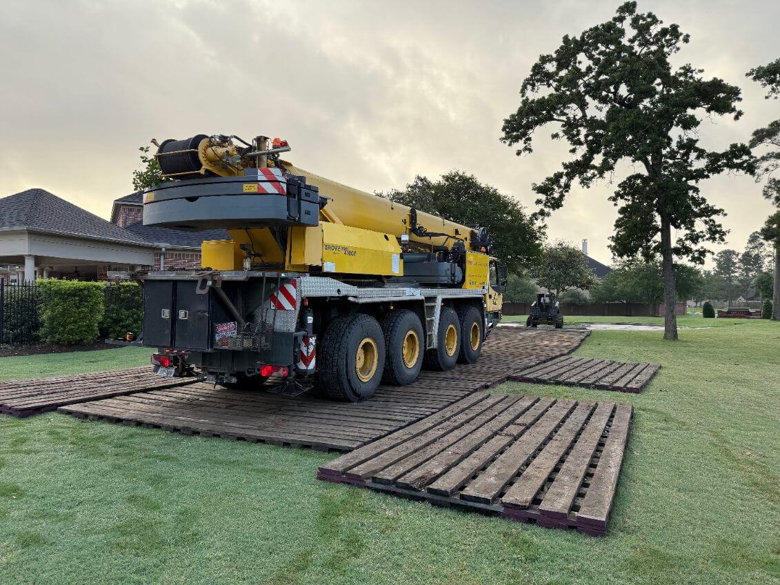 Yellow crane on construction laminated mats protecting grass.